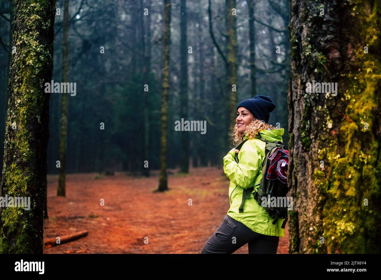 Happy female excursionist enjoy nature background and forest around smiling and resting against a tree. Travel backpacker woman in outdoor leisure Stock Photo