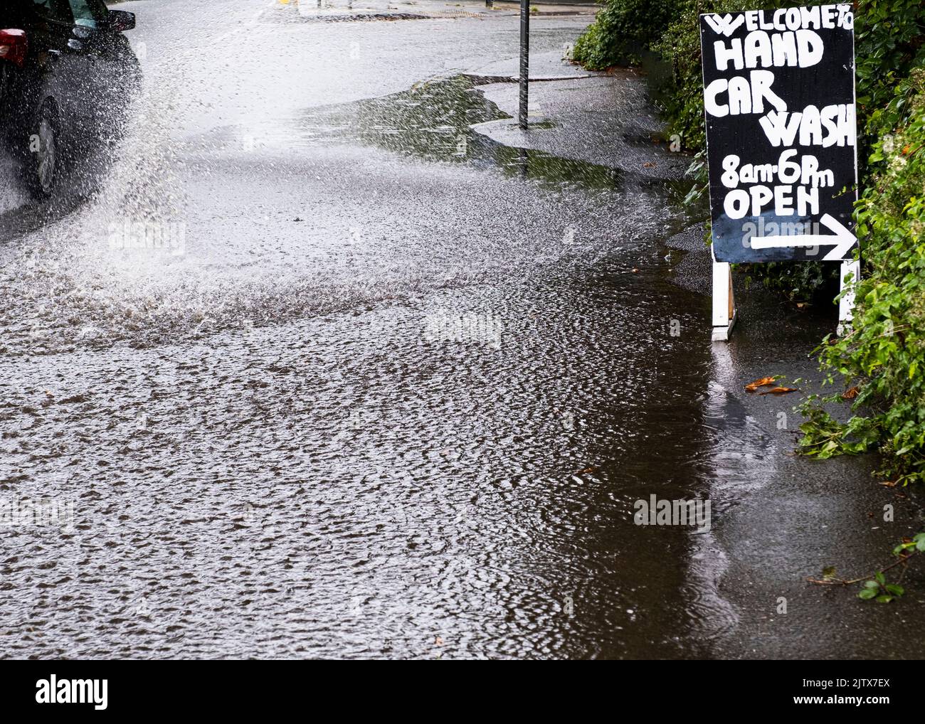 A car splashing standing flood rainwater on a road during a rain storm by a car wash sign Stock Photo