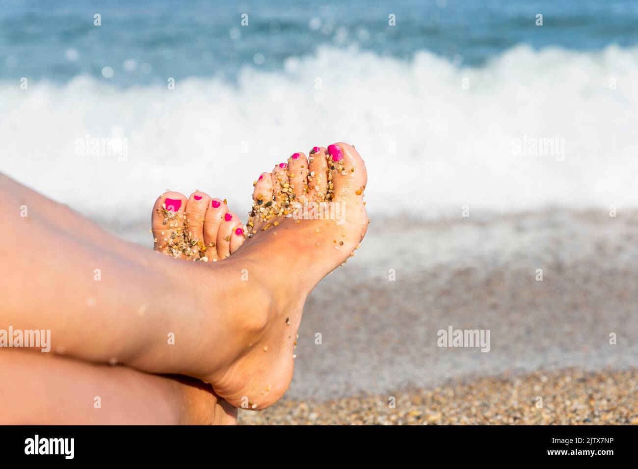 Woman feet closeup on a beach. Pink nails on toes. Enjoying sun on sunny summer day by the water. Stock Photo
