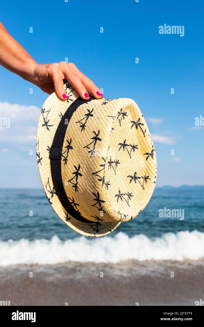 Woman holding straw sun hat at sunny beach at sea. Travel and fashion concept. Stock Photo