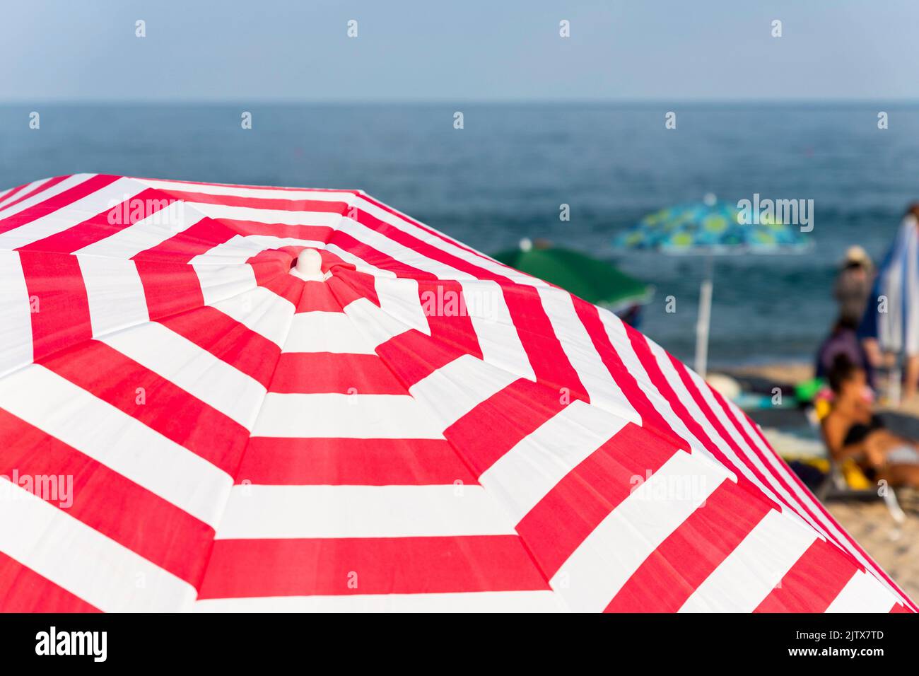 Striped beach umbrella at the beach with tourists and sea in background. Stock Photo