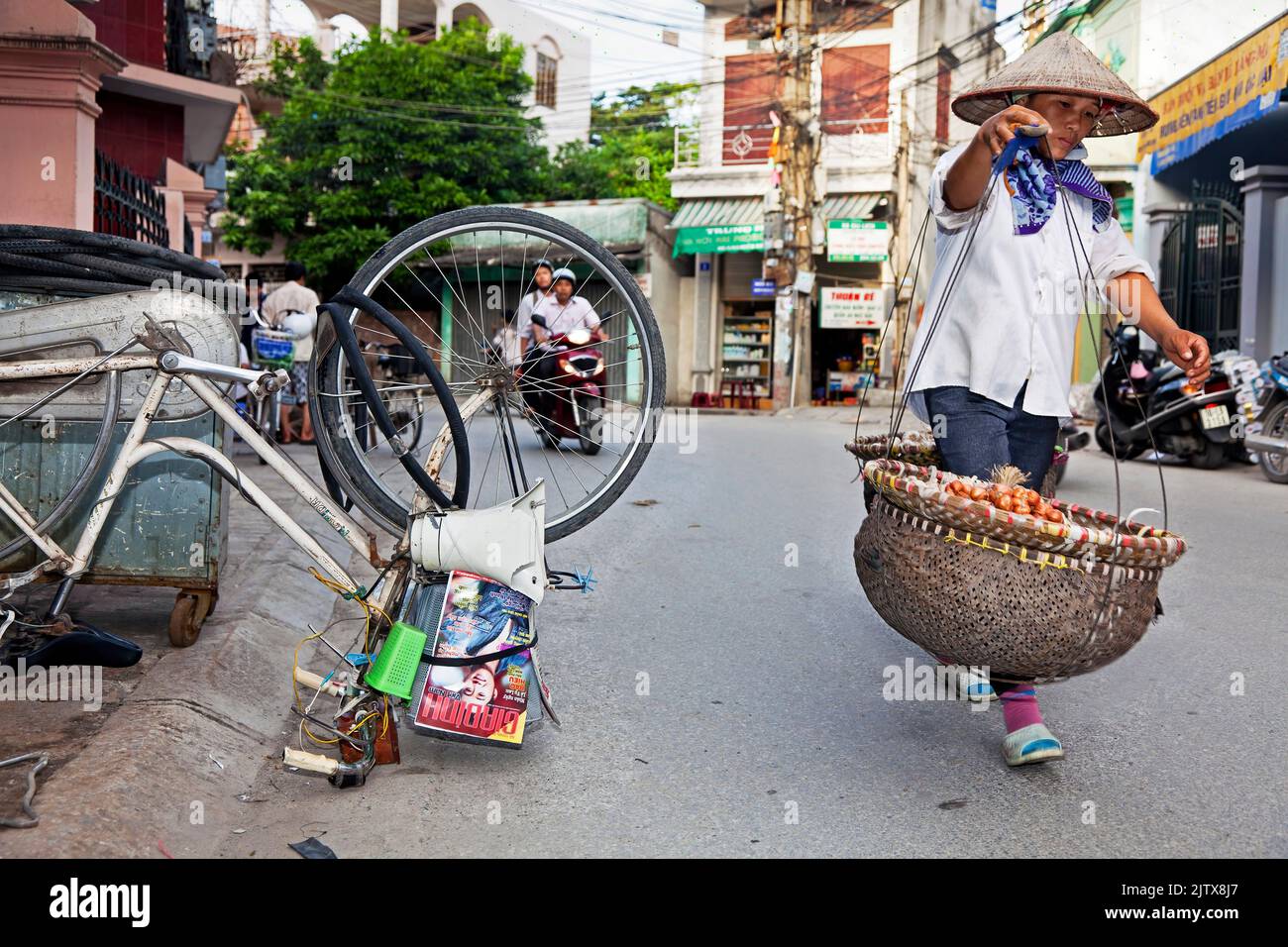 Vietnamese street vendor carrying pannier baskets, and bicycle repair in the road, Hai Phong, Vietnam Stock Photo