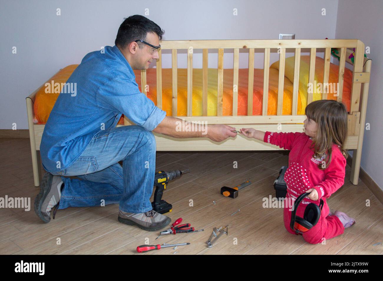 Picture of an adorable little girl helping her handyman dad to fit the fall protector to the bed. Do it yourself work Stock Photo