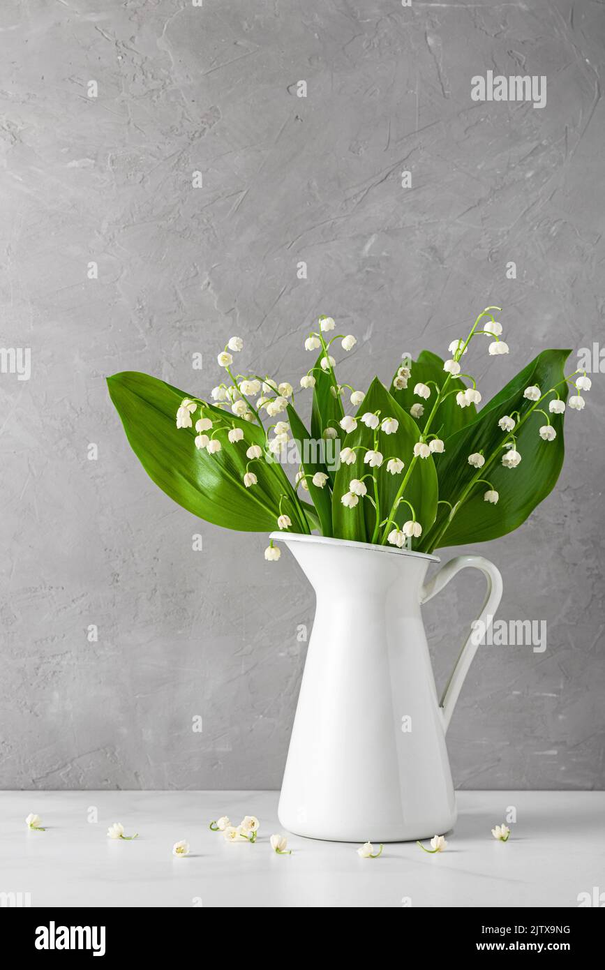 Still life with lily of the valley flowers bouquet in vase on gray concrete background. Vertical orientation. Wedding or holiday concept Stock Photo