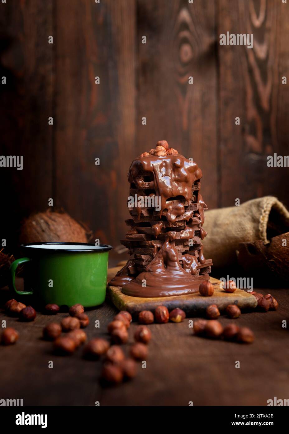 Hot chocolate in the mug and stack of chocolate bars with melted chocolate cream dripping over it in the rustic kitchen. Stock Photo