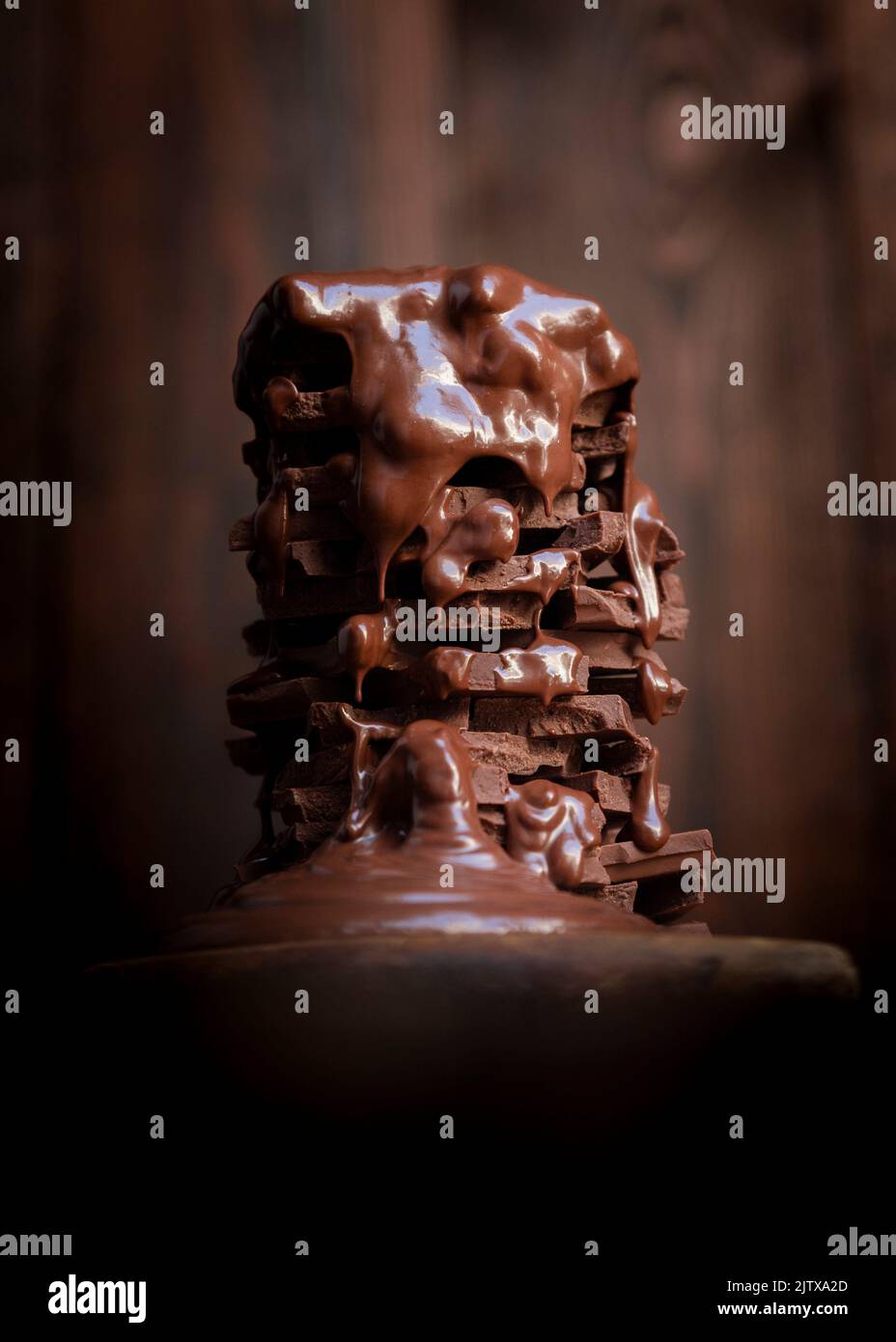 Melted hot chocolate dripping over a pile of chocolate bars on a rustic wooden table. Stock Photo
