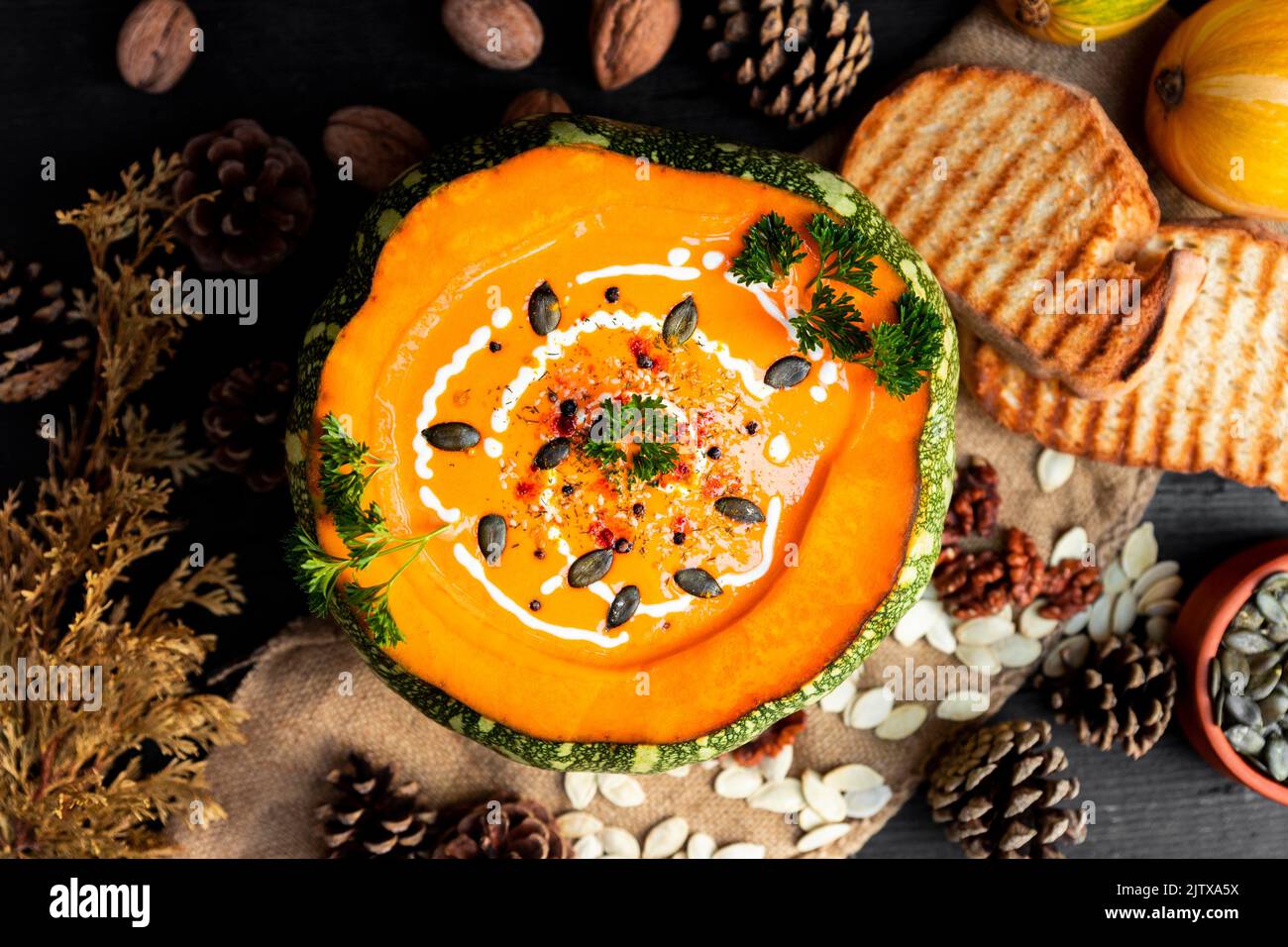 Pumpkin soup with pumpkin seeds, cream, parsley and spices on the rustic kitchen table. Flat lay. Top view photo. Stock Photo