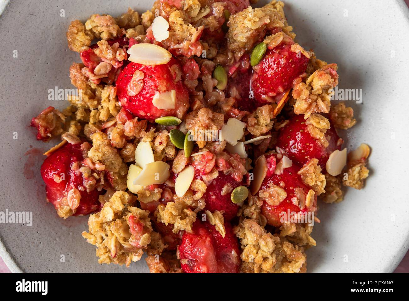 Close up of delicious strawberry crumble with almonds and pumpkin seeds in a plate. Top view. Tasty breakfast Stock Photo
