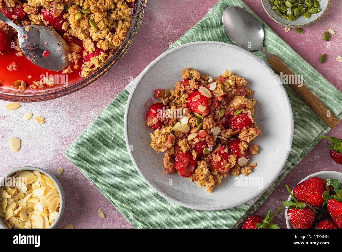 Strawberry crumble with almonds in a plate with spoon on pink background. Top view. tasty breakfast. Delicious food Stock Photo