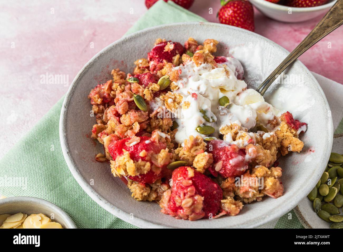 Strawberry crumble with ice cream and almonds in a plate with spoon on green napkin over pink background. tasty breakfast. Delicious food Stock Photo