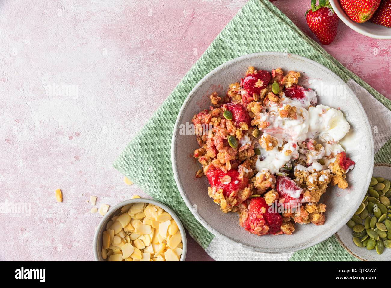 Delicious strawberry crumble with ice cream, almonds and pumpkin seeds in a plate on pink background. Top view with copy space. Tasty breakfast Stock Photo