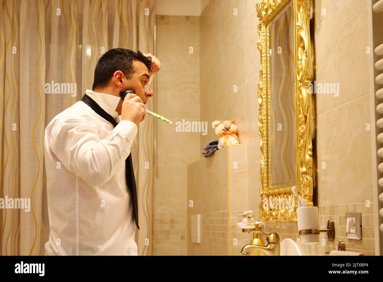 businessman in bathroom late for work while combing, brushing teeth and shaving at the same time Stock Photo