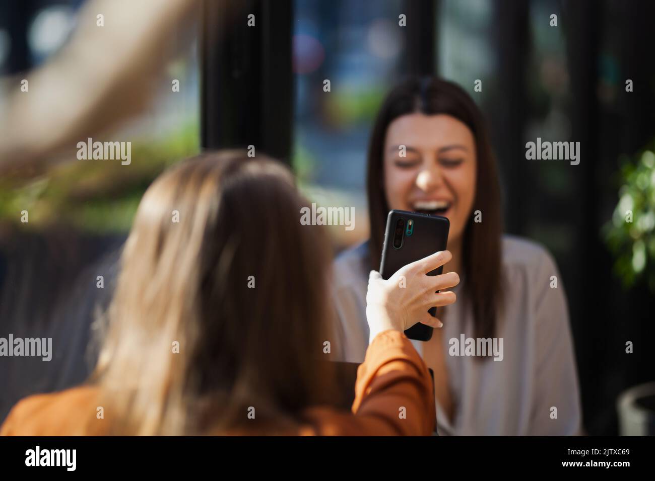 Two young business women in a cafe having one on one meeting. Friends after work talking gossiping and having coffee at a window table with reflection Stock Photo