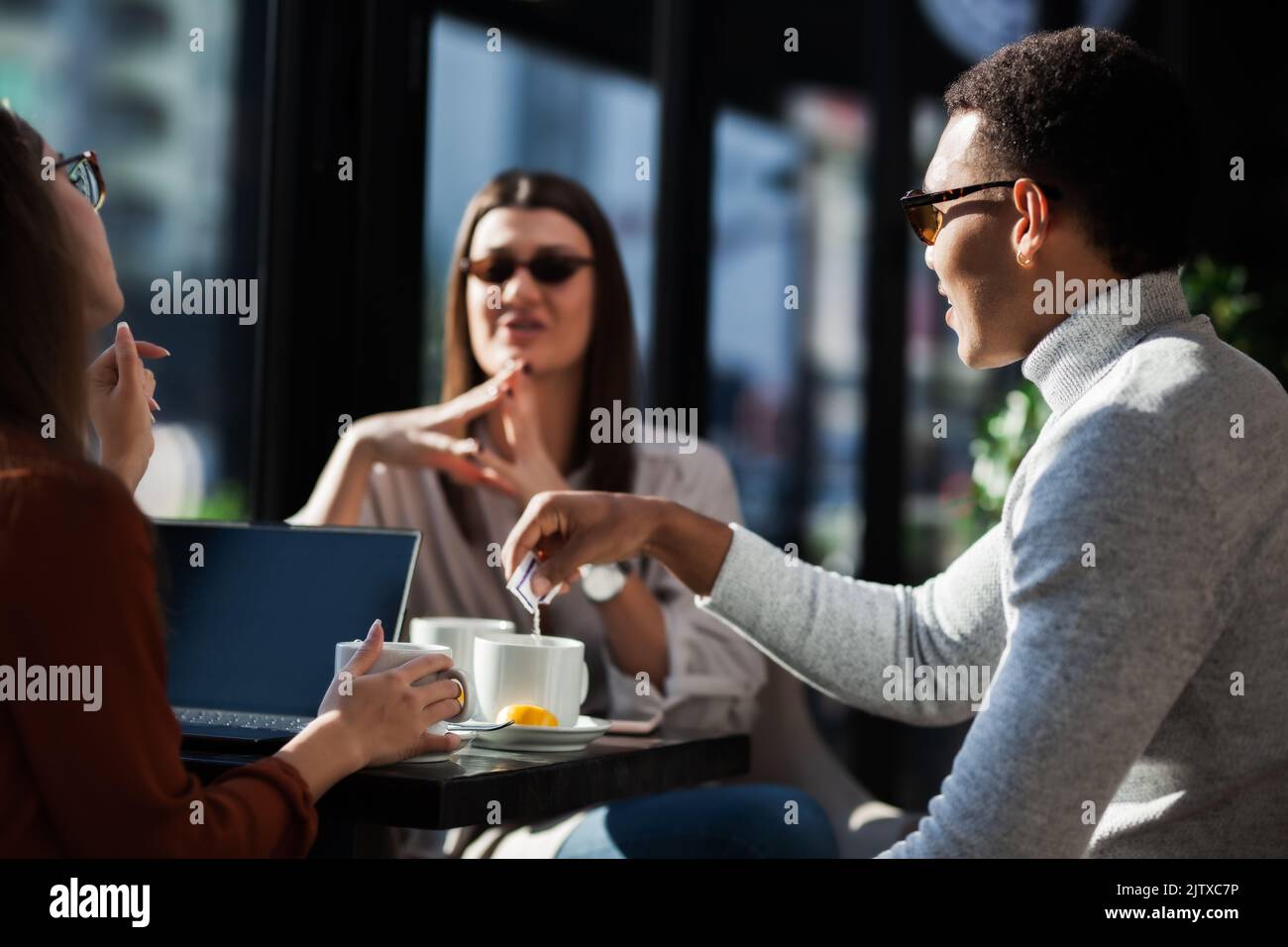 Three friends in a restaurant talking smiling and drinking tea. Business colleagues having a meeting after work or during coffee break at a cafe bar. Stock Photo