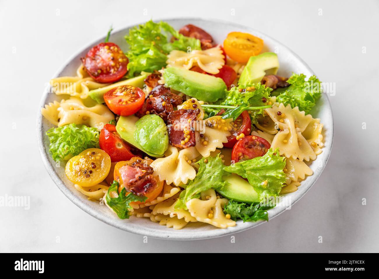 Pasta farfalle salad with tomato, bacon, avocado and mustard dressing in a plate on white table. Close up. Healthy italian food Stock Photo