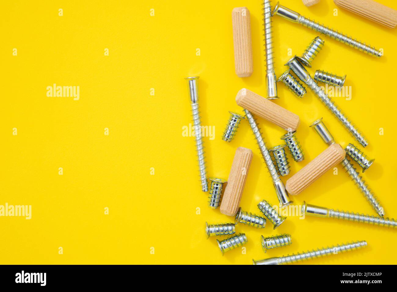 Steel screws and wooden dowels for furniture different types on yellow background. Top view Stock Photo