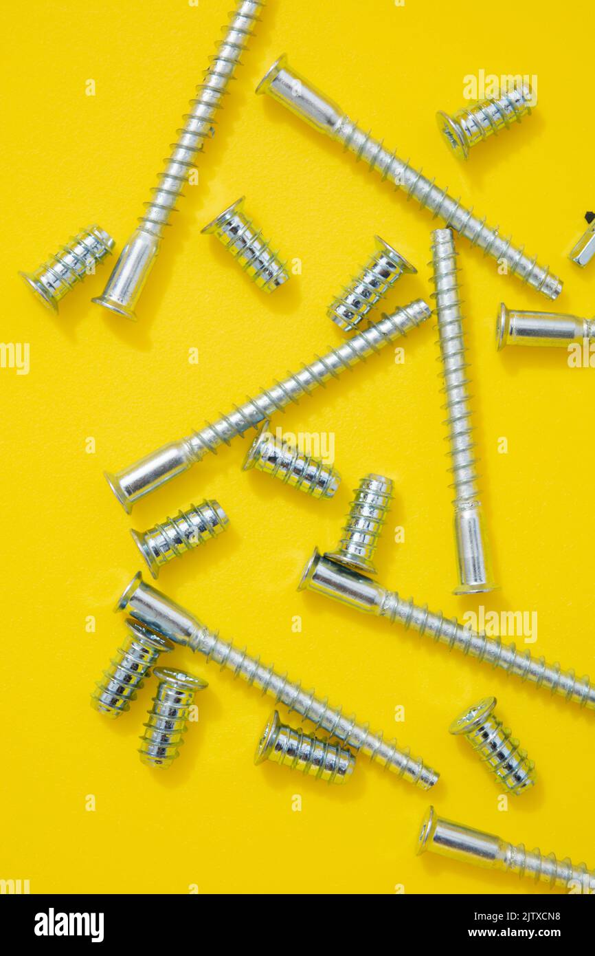 Steel screws for furniture different types on yellow background. Top view Stock Photo