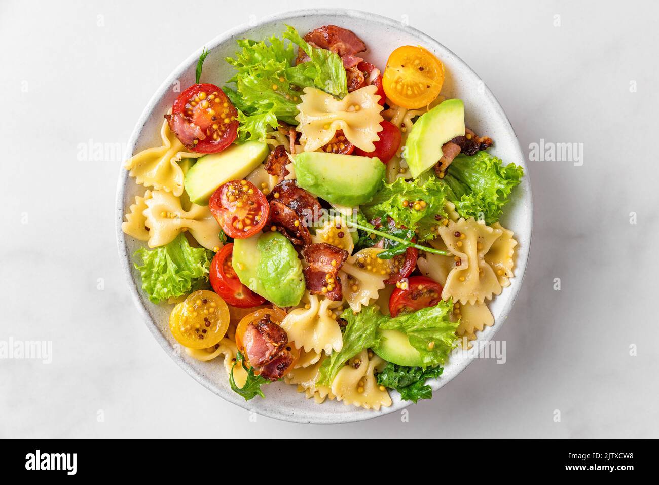 Pasta farfalle salad with tomato, bacon, avocado and mustard dressing in a plate on white table. Top view. Healthy italian food Stock Photo