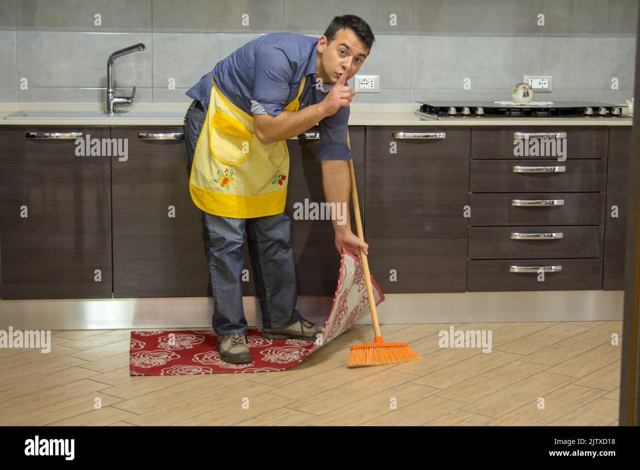 boy doing housework while making a gesture of silence and hiding dirt under the carpet Stock