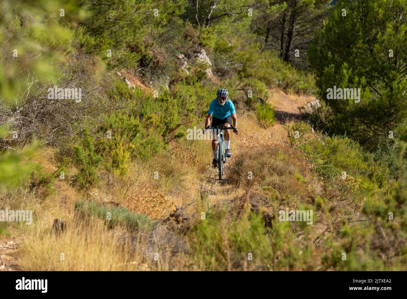 A male cyclist in a mediterranean forest gravel road bicycle ride in the Costa Blanca, Alicante, Spain Stock Photo