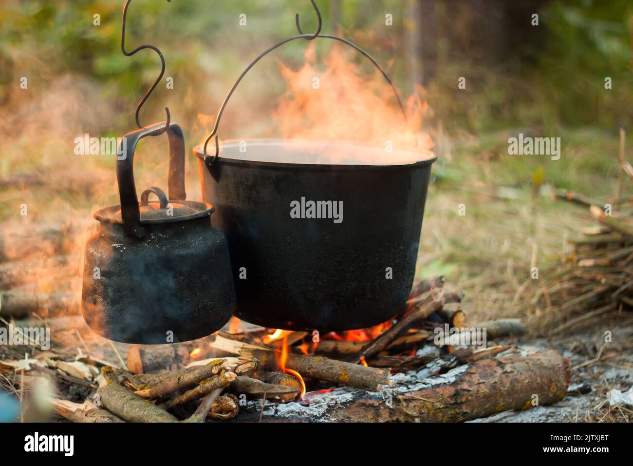 Two smoked tourist kettles over camp fire. Process of cooking on the