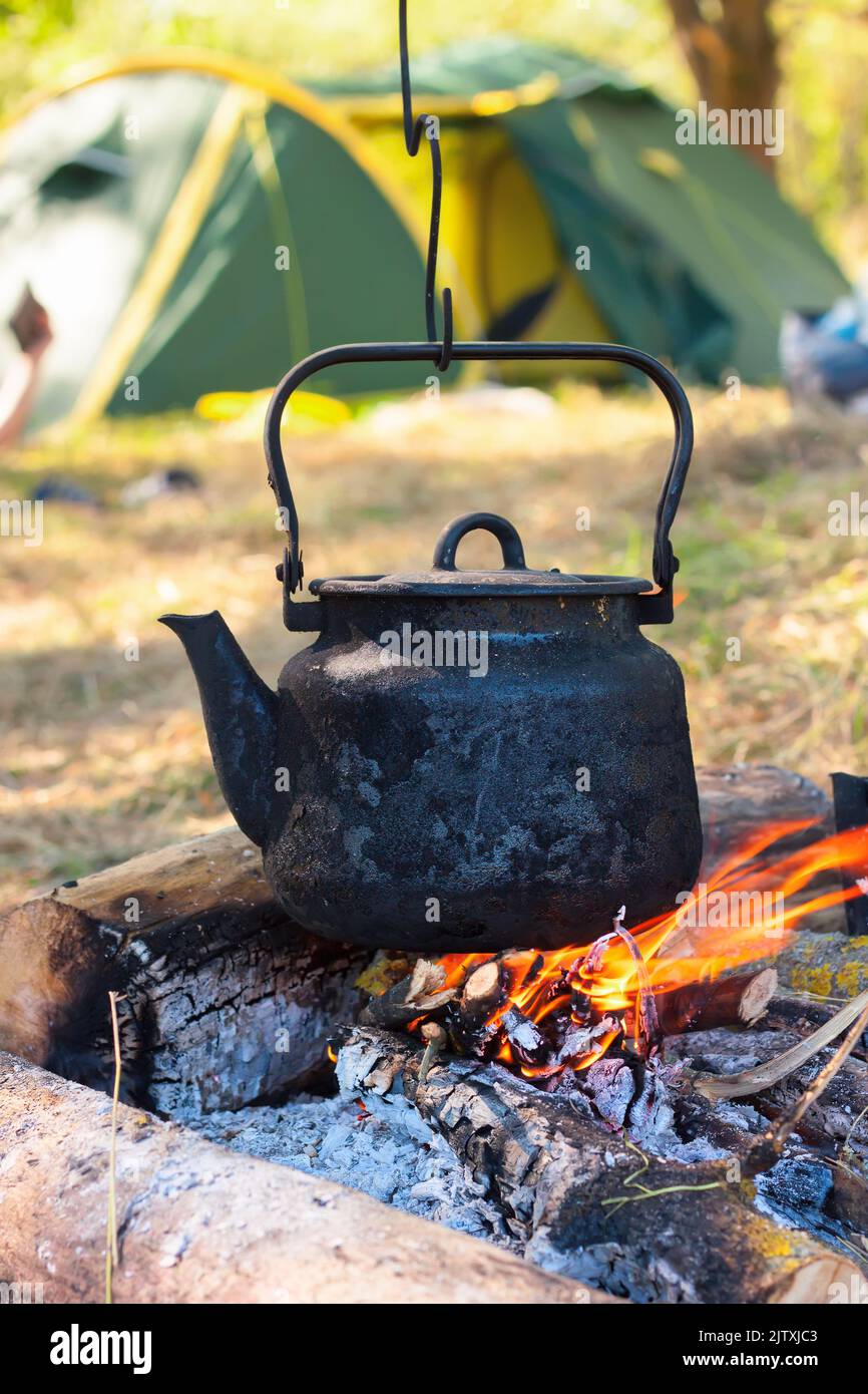 Smoked tourist kettle over camp fire. Process of cooking on the nature. Stock Photo