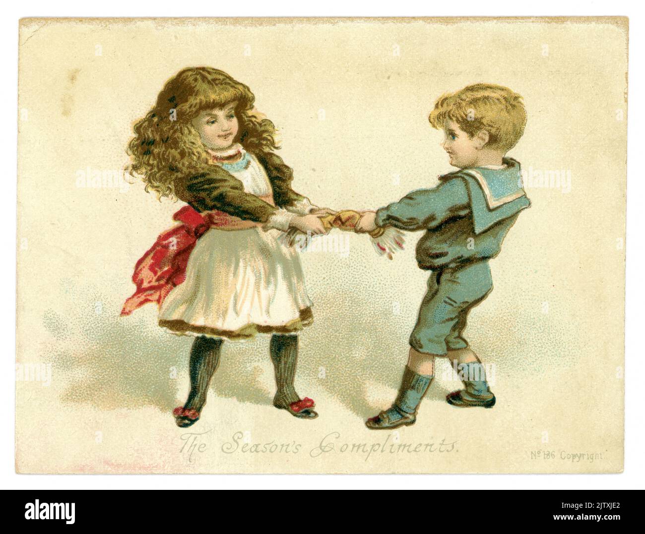Original, charming Victorian Christmas card, greetings card of young Victorian boy and girl pulling a cracker. The boy is dressed in a sailor suit, the girl has long hair in waves, the caption is 'The Season's Compliments', dated 1887, U.K. Stock Photo