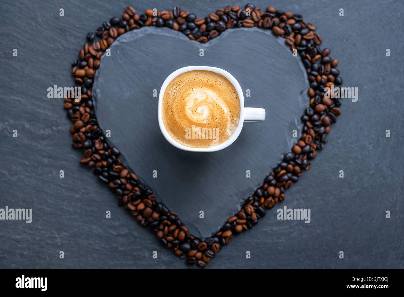 Delicious cup of coffee on a heart made of slate rimmed with coffee beans Stock Photo