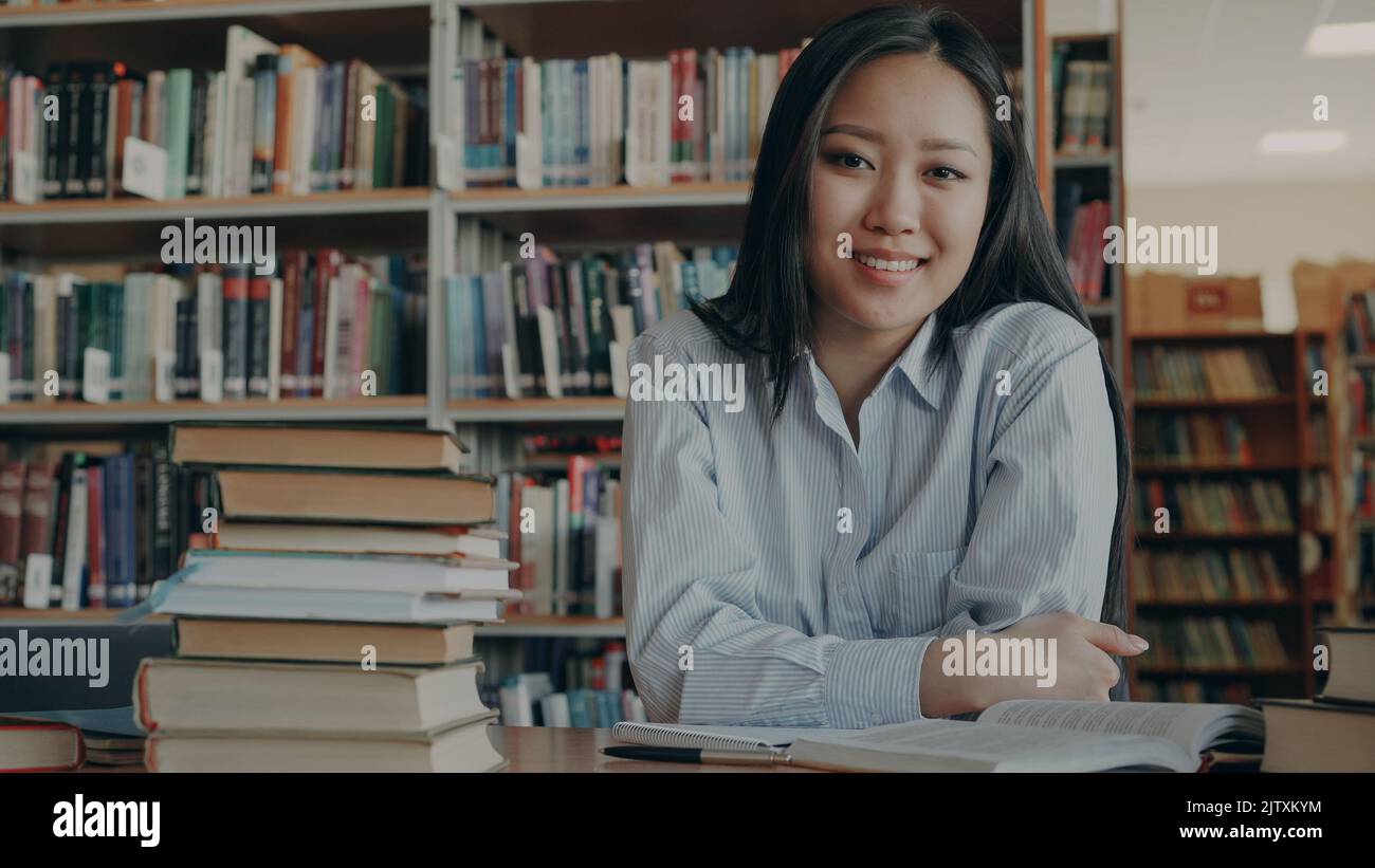 Portrait of young beautiful asian female student sitting at table with ...