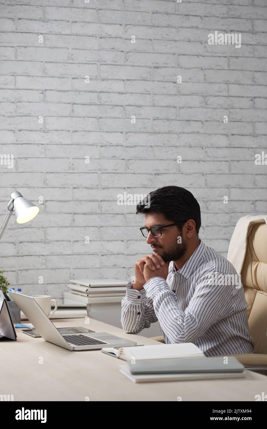 Pensive Indian man looking at information on laptop screen Stock Photo
