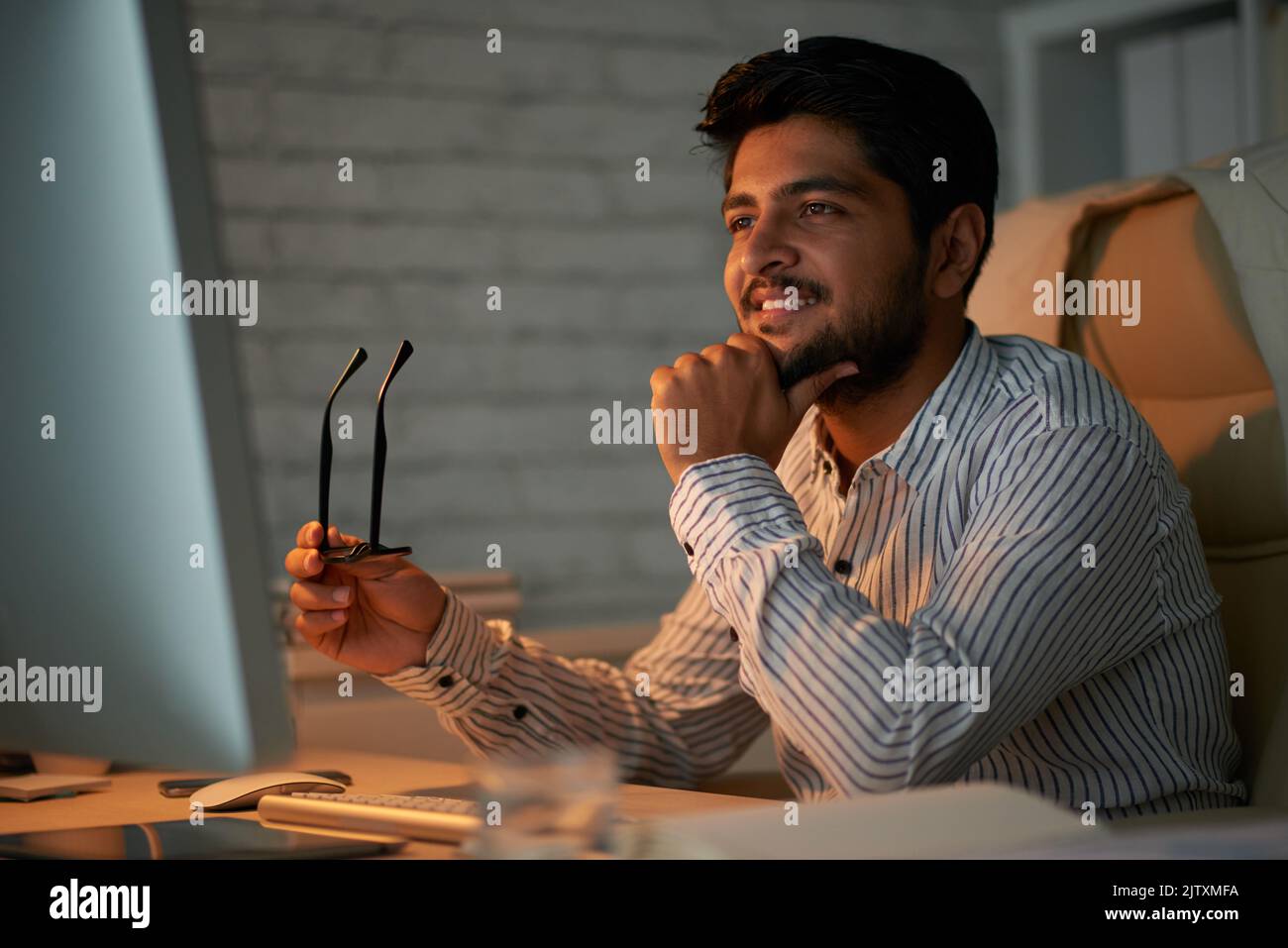 Smiling handsome Indian entreprenur reading information on computer ...