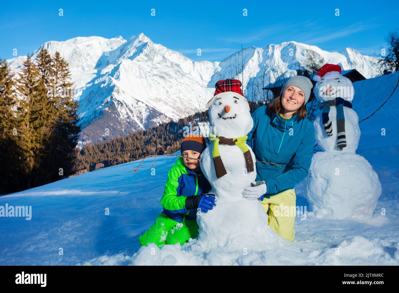 Boy and mother playing with newly made snowman in the mountains Stock Photo