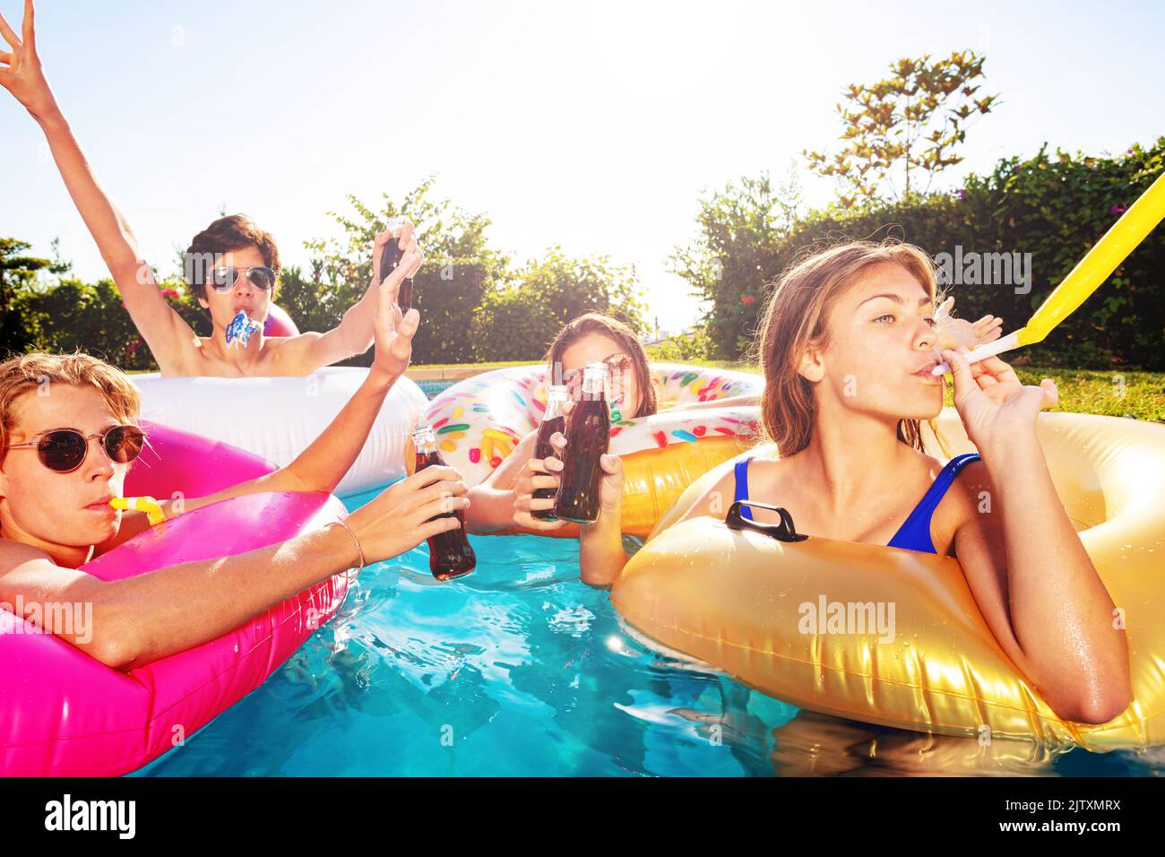 Teenage children blow noisemaker in swimming pool Stock Photo