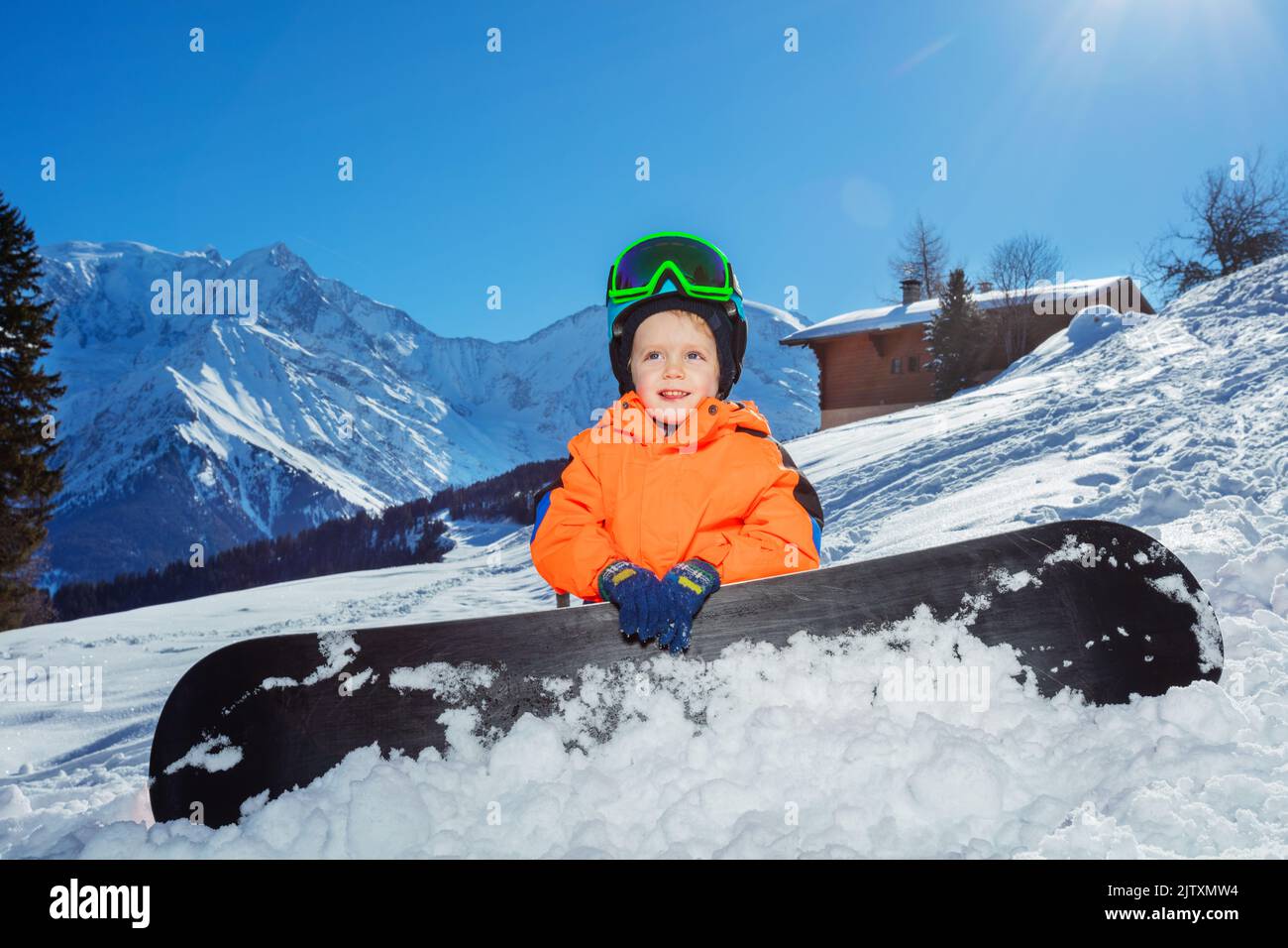Happy little boy sit with snowboard on alpine ski track Stock Photo