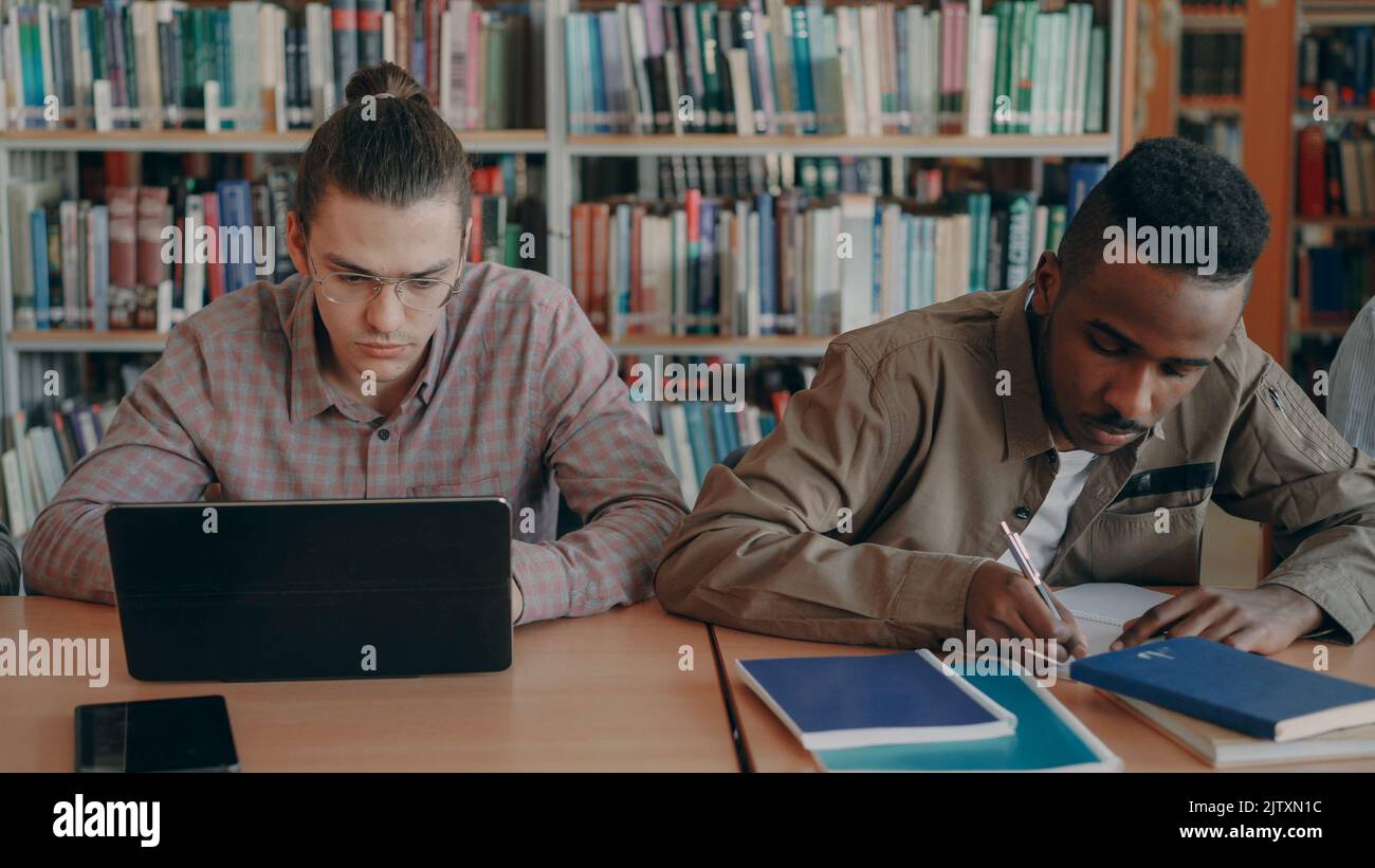 Two concentrated students preparing for examination while sitting at table in university library indoors Stock Photo