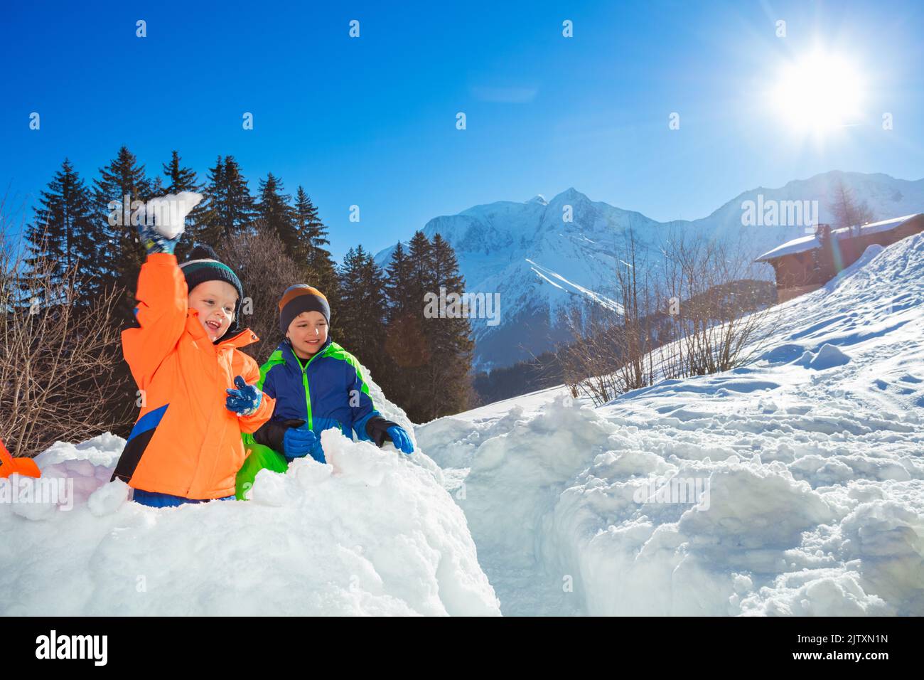Two boys play snowball in the snow fortress over mountains Stock Photo