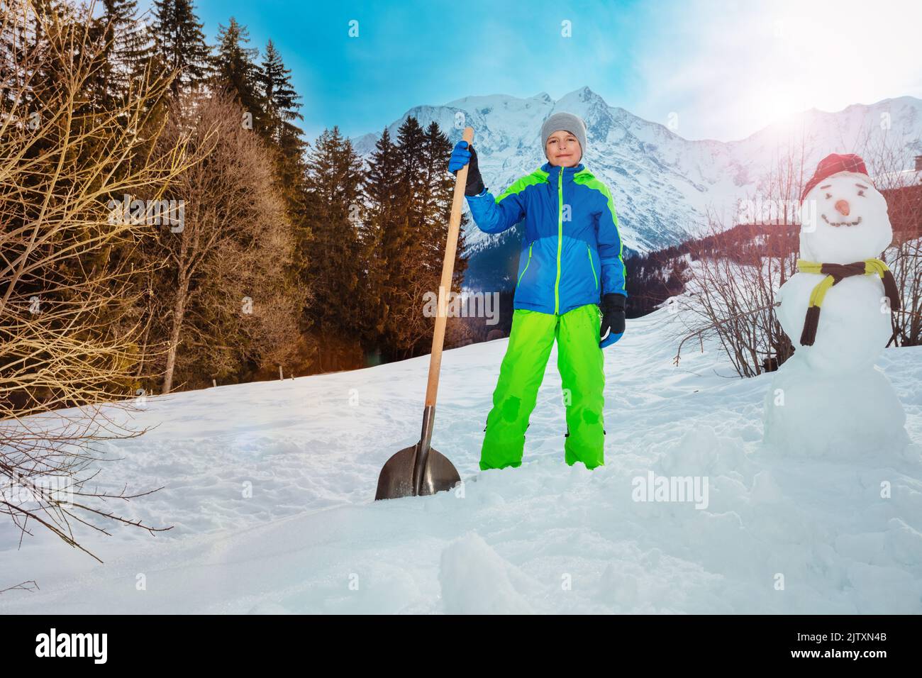 Child stand with shovel clean snow and building a snowman Stock Photo