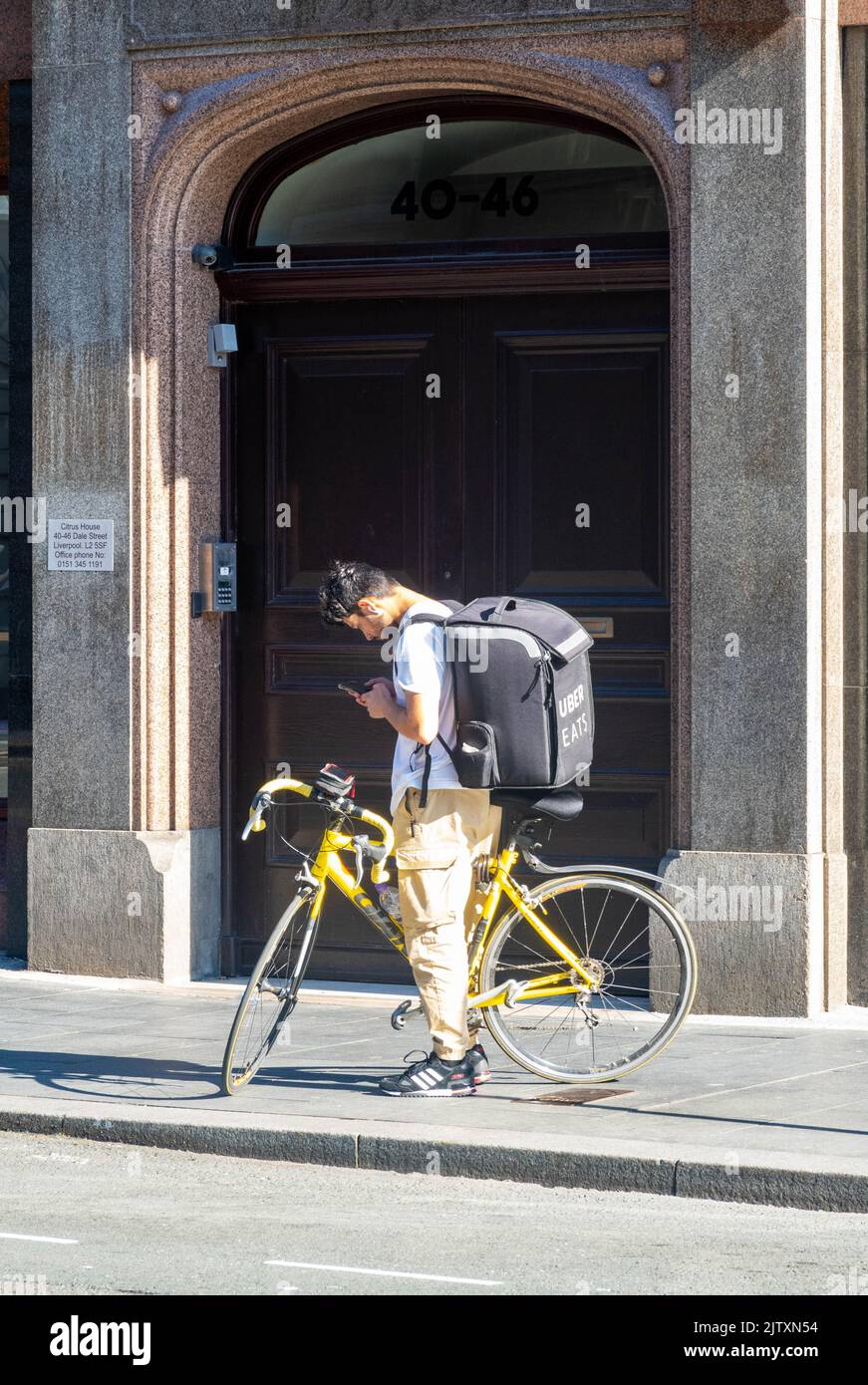 Young Uber Eats bike delivery man checking his cell phone for deliveries Stock Photo
