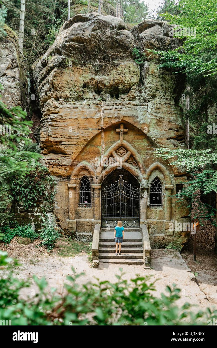 Woman traveler in Prayer Valley, Modlivy dul,with chapel carved into rock.Deep rocky valley covered with forest and sandstone rocks near Svojkov Stock Photo