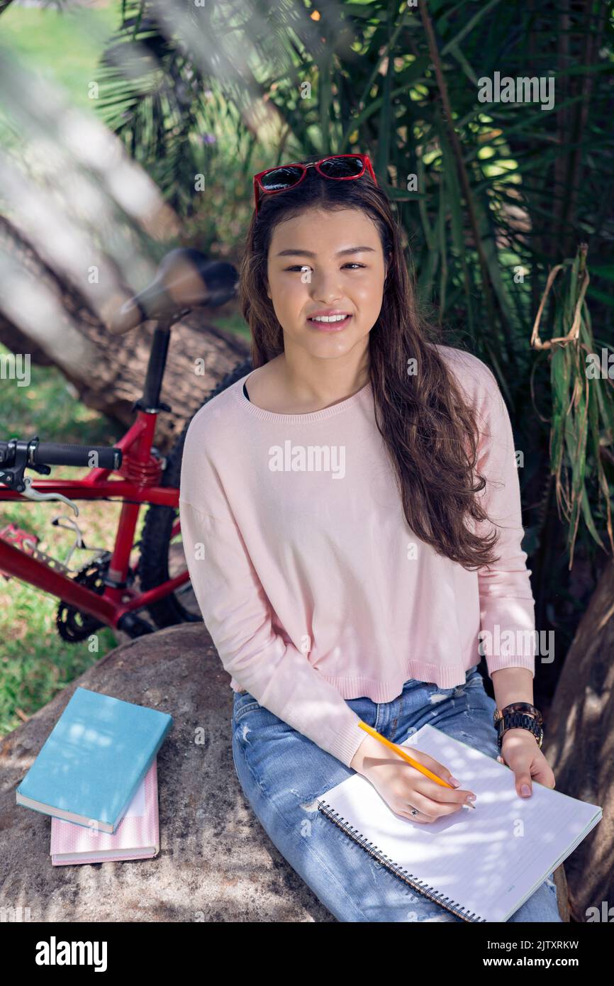 Pretty mixedrace college student writing in her textbook Stock Photo