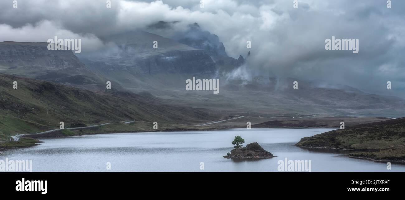 Clouds rolling over Old Man of Storr on Isle of Skye, Scotland, UK. Painterly, panoramic landscape scene with moody sky over mountain and lake with is Stock Photo