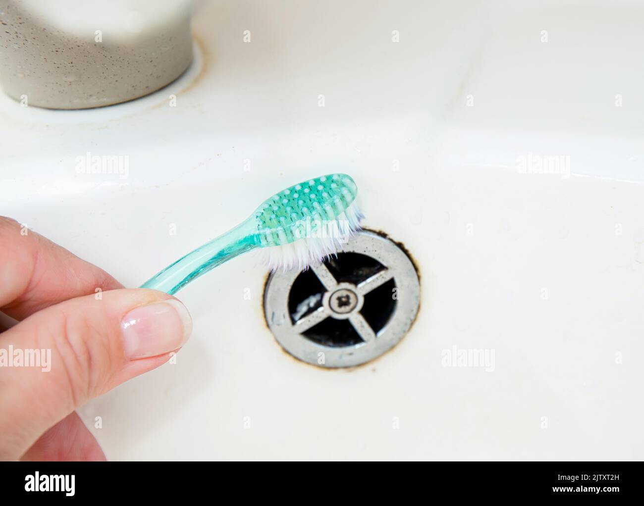 Close up view of woman hand cleaning bathroom sink with toothbrush. Home cleaning hack, fits small spaces to clean off mould and dirt. Stock Photo
