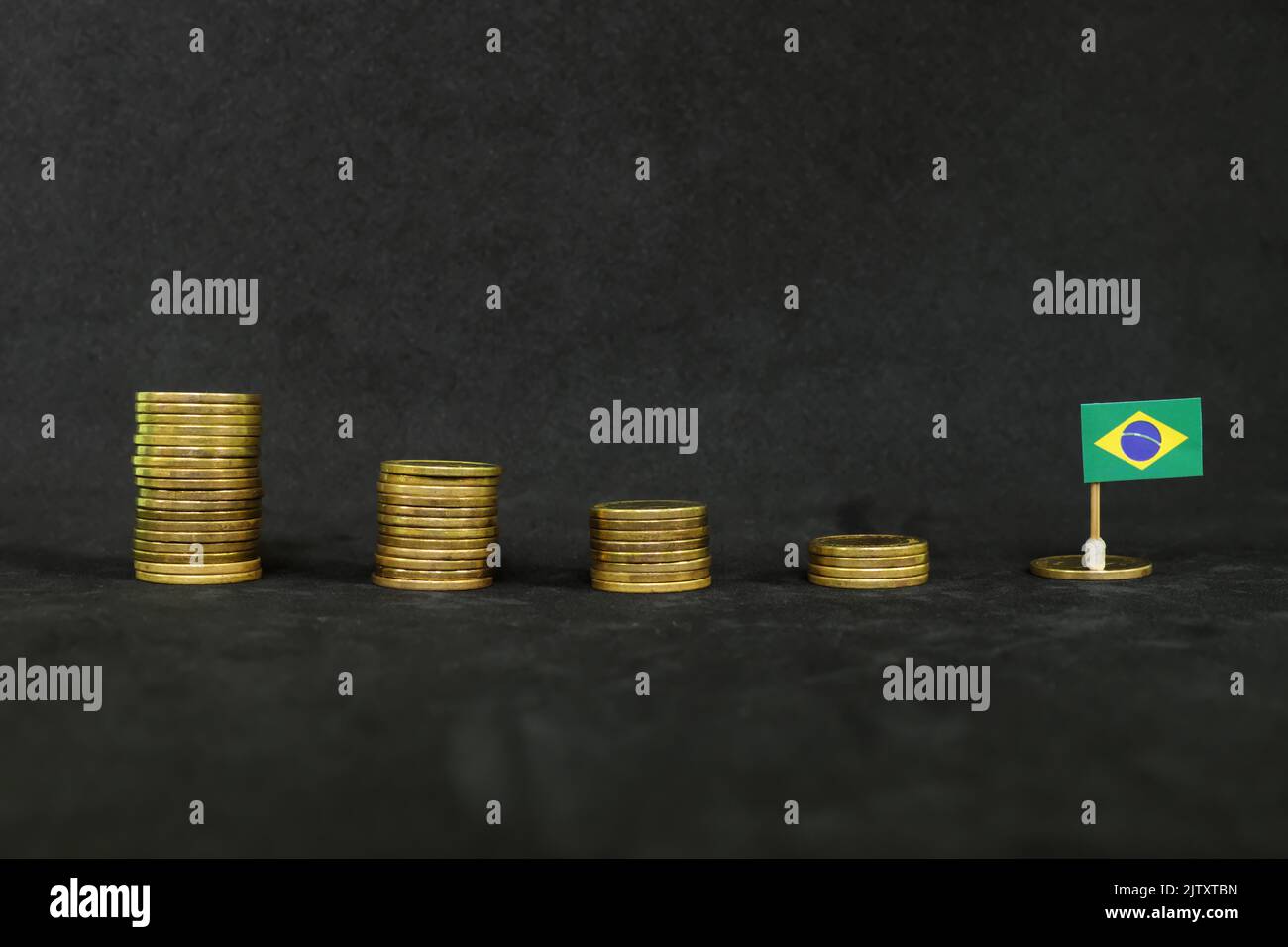 Brazil economic recession, financial crisis and peso depreciation concept. Brazilian flag in decreasing stack of coins in dark black background. Stock Photo