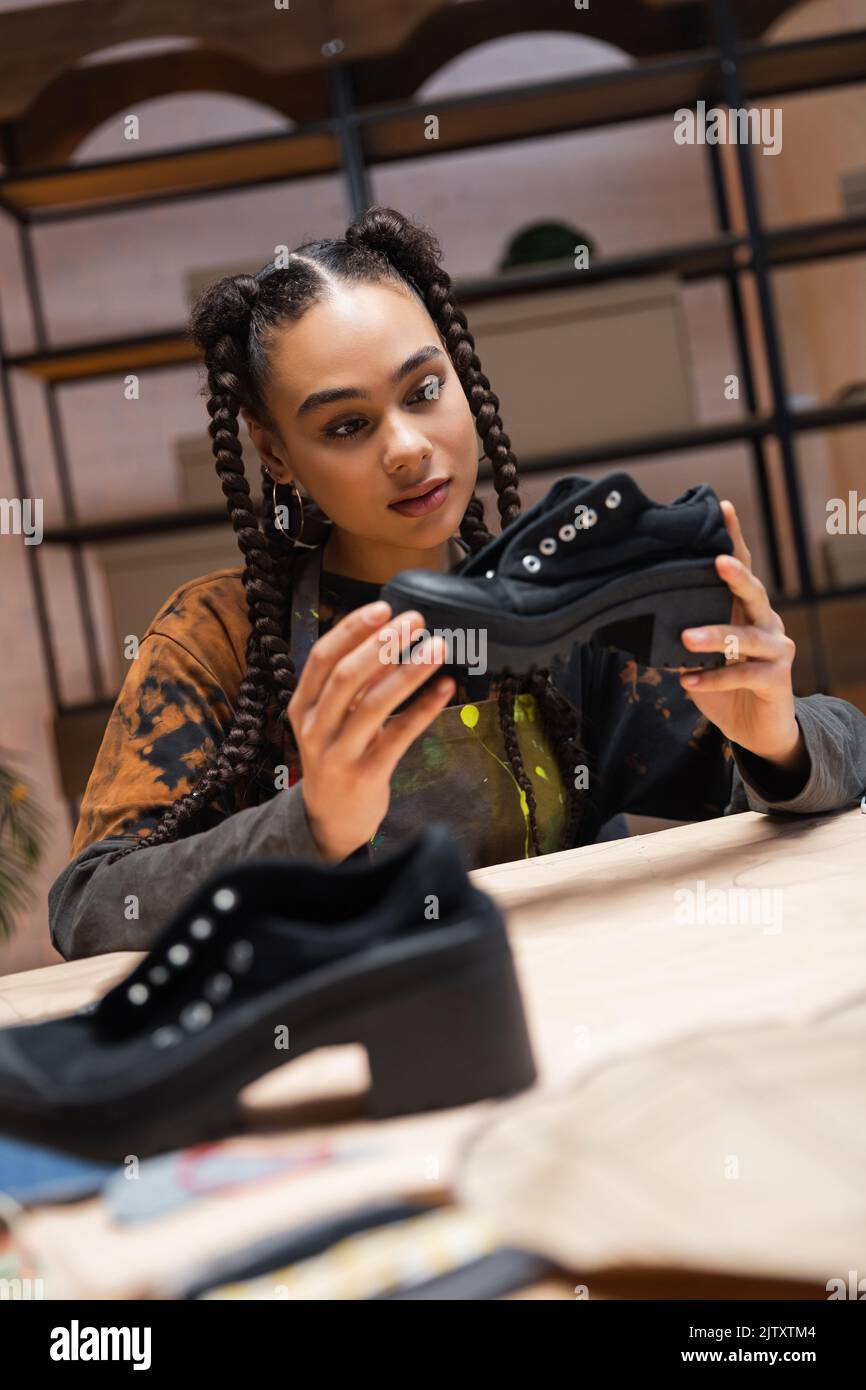 African american craftswoman holding shoe near blurred sewing pattern in workshop,stock image Stock Photo