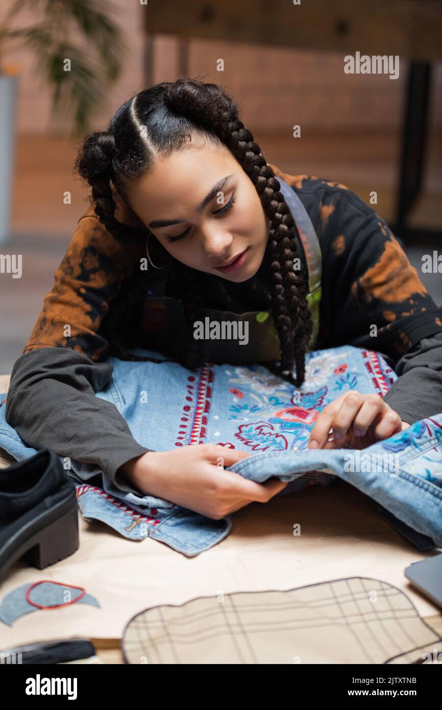 African american designer embroidering denim jacket in workshop,stock image Stock Photo
