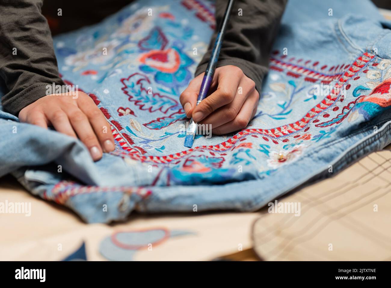 Cropped view of african american designer painting on denim jacket near blurred sewing pattern,stock image Stock Photo