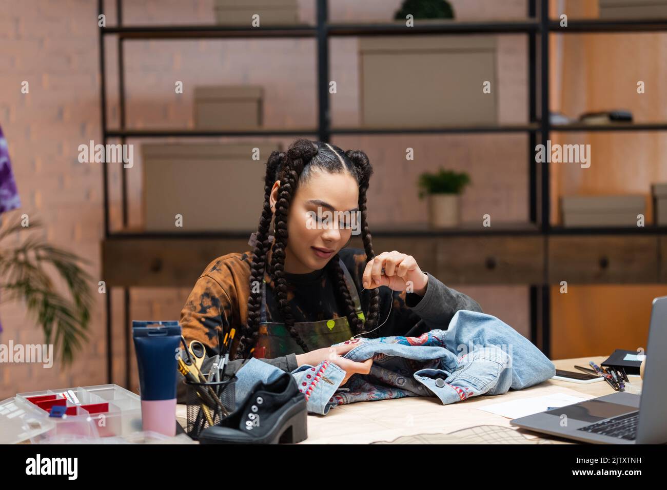 African american designer embroidering denim jacket near devices in workshop,stock image Stock Photo