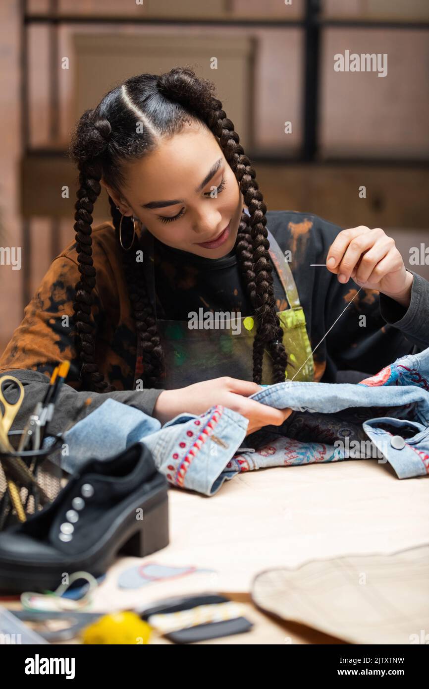 Young african american craftswoman embroidering denim jacket in workshop,stock image Stock Photo