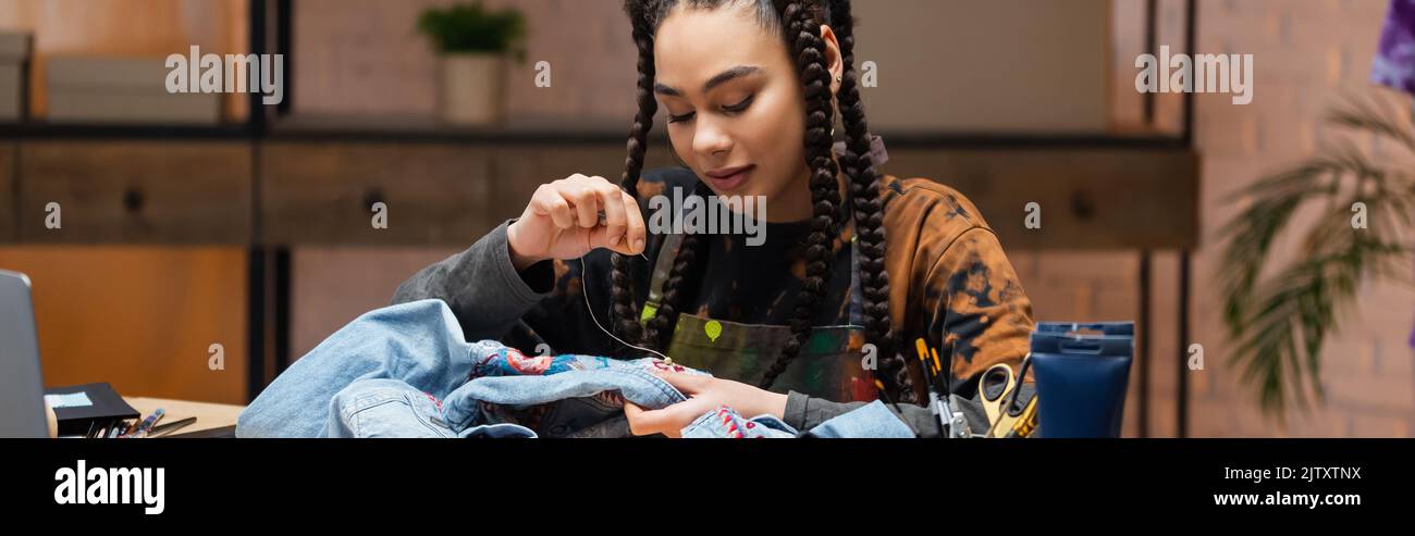Young african american designer embroidering denim jacket in workshop, banner,stock image Stock Photo