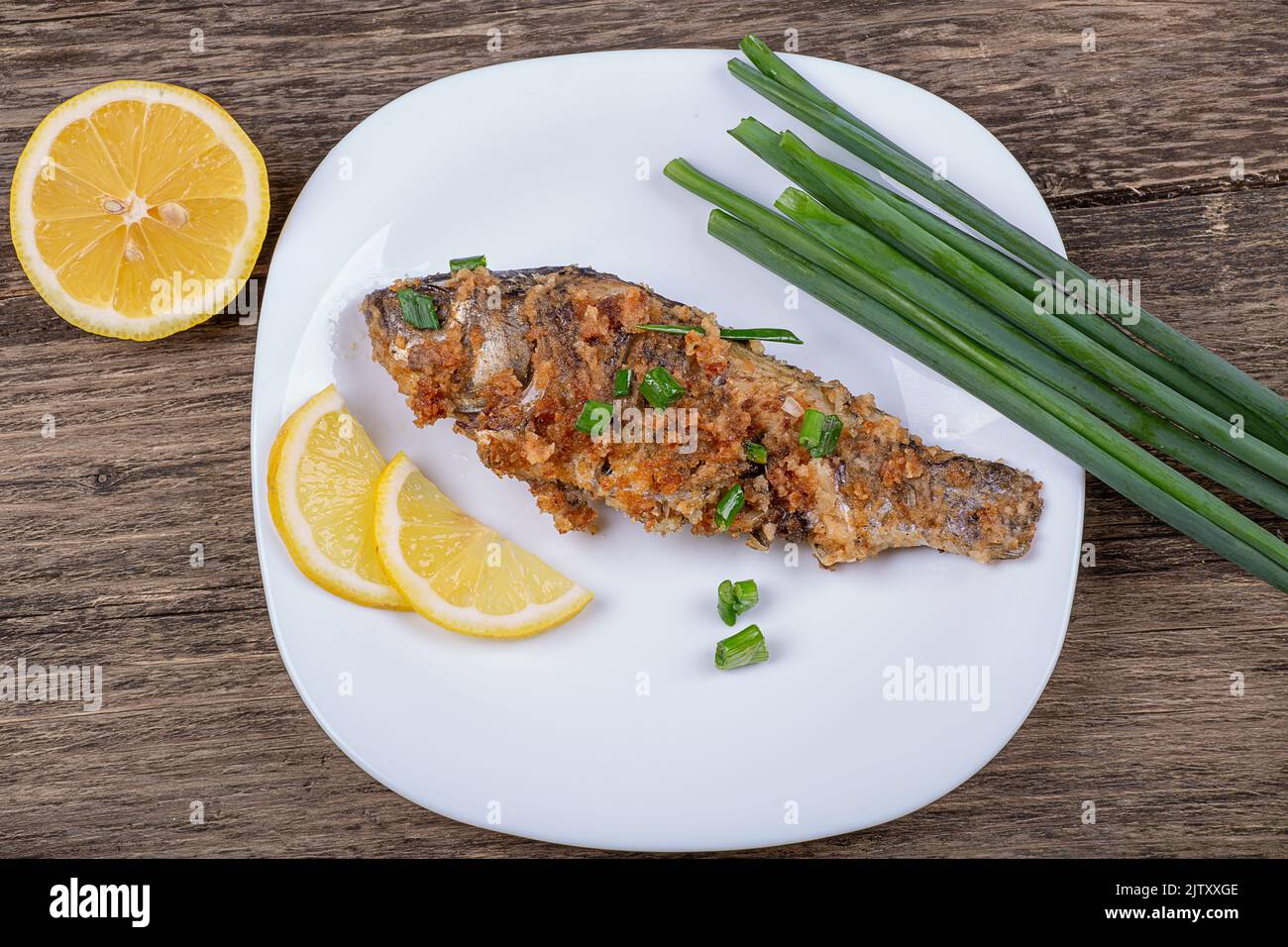 Fried breaded fish with green onions and lemon, in a plate on an old